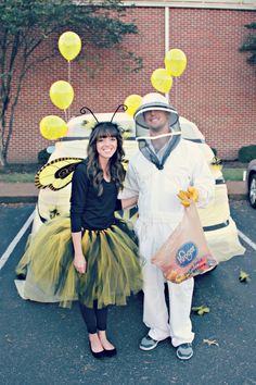 a man and woman dressed in costumes standing next to a car with balloons on it