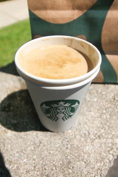 a cup of coffee sitting on top of a table next to a brown paper bag