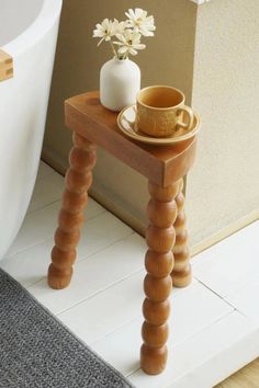 a small wooden table with a cup and saucer on it next to a toilet