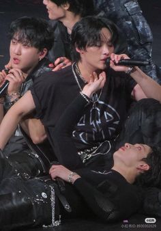 group of young men sitting on the ground with microphones in their hands and wearing black clothing