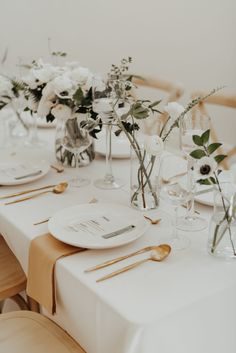 the table is set with white and gold place settings, flowers in glass vases