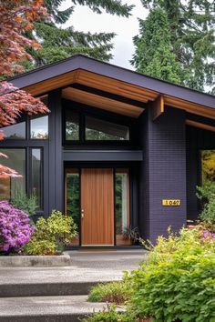 a black house with wooden doors and windows in the front yard, surrounded by trees