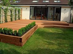 a wooden deck in the middle of a yard with plants growing on it's sides