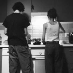 two people are standing in the kitchen preparing food on the stove top and countertop