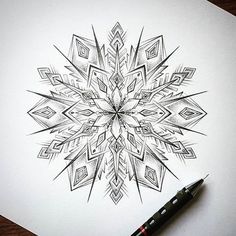 a drawing of a snowflake on paper next to a black marker and pen