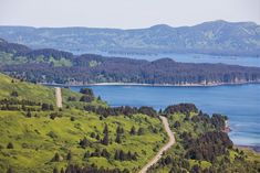 an aerial view of a road winding through the green hills and lakes in the distance