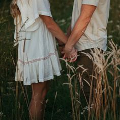 a man and woman holding hands while standing in tall grass