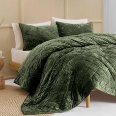 a bed with green comforter and pillows on top of it in front of a white wall