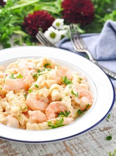 a white plate topped with pasta covered in shrimp and parsley next to a fork