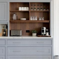 a kitchen with gray cabinets and white counter tops, coffee maker on the far wall