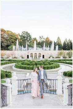 a man and woman standing next to each other in front of a formal garden area