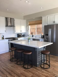 a kitchen with an island and three stools in it, along with stainless steel appliances