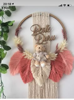 a wall hanging with a teddy bear in the middle of it and some plants behind it