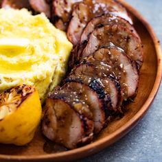 a wooden plate topped with meat, potatoes and mashed potatoes