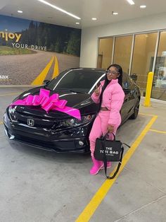 a woman sitting on the hood of a black car with a pink ribbon around it