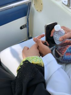 a person sitting on a boat using a cell phone while holding a water bottle in their hand