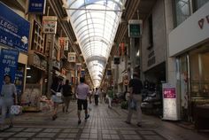 people are walking down an indoor shopping mall with glass ceiling and skylights above them