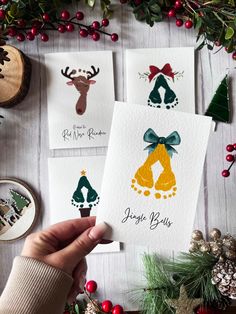 handmade christmas cards with reindeers and bells on them, surrounded by evergreen branches