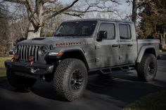 a gray jeep is parked on the side of the road in front of some trees