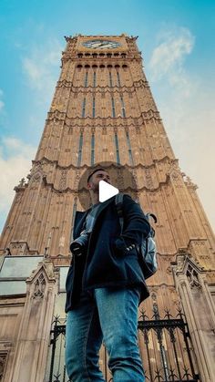 a man standing in front of a tall tower with a clock on it's side