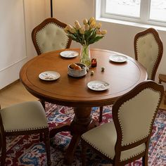 a dining room table with chairs and plates on it, in front of a window