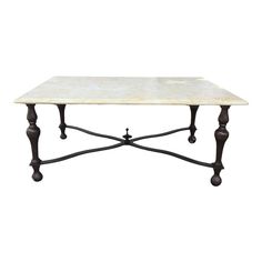 a white marble top coffee table with black iron legs and an ornate design on the base