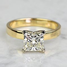 a yellow gold engagement ring with a princess cut diamond in the center on a marble surface