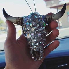 a hand holding a fake bull's skull with lots of crystals