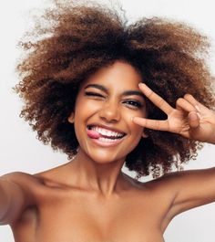 a woman smiling and making the peace sign with her hand while wearing a white tube top