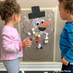 two children standing in front of a paper snowman