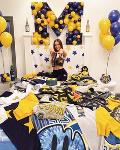 a woman sitting on top of a bed surrounded by yellow and blue balloons