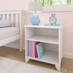 a white book shelf sitting next to a bed in a room with pink wallpaper