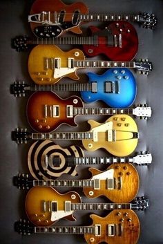 guitars are lined up on the wall in a row, all different colors and sizes