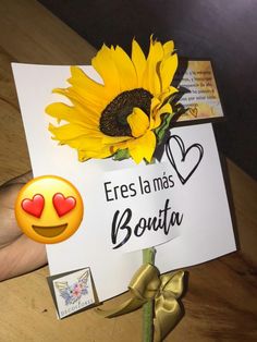 a yellow sunflower sitting on top of a table next to a sign with a smiley face