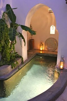 an indoor swimming pool surrounded by greenery and lanterns with candles on either side at night