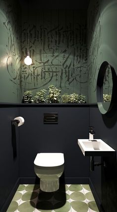 a white toilet sitting next to a sink in a bathroom under a round mirror on the wall