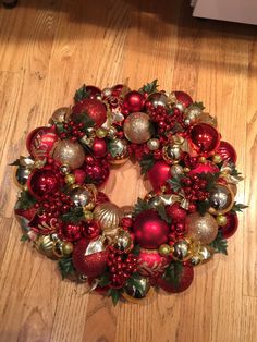 a red and gold christmas ornament wreath on a wooden floor