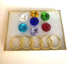 six pairs of rings with different colored stones in a display box on a white surface