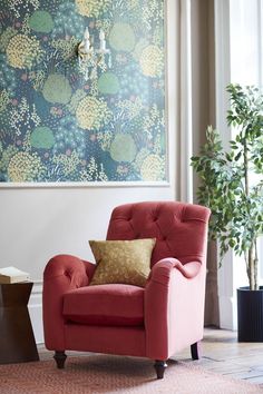 a red chair sitting in front of a window with a painting on the wall behind it