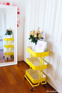 a room with a mirror, yellow cart and flowers on the table in front of it