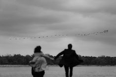 two people are flying kites in the sky on a cloudy day with birds above them