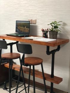 a laptop computer sitting on top of a wooden desk next to two stools and a potted plant