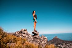 a woman standing on top of a rock near the ocean