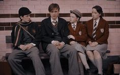 four young men sitting on a bench in front of a brick wall, one wearing a suit and tie