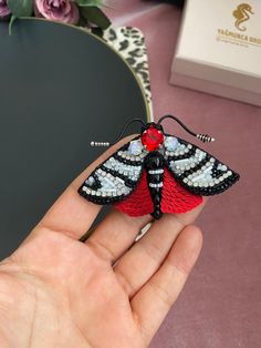 a small red and black butterfly brooch sitting on someone's finger