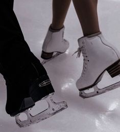 two people wearing ice skates standing in the snow with their feet on each other