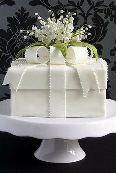 a square cake with white frosting and flowers on top is sitting on a pedestal