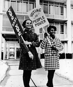 two women holding signs in front of a building with snow on the ground and buildings behind them