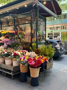 an outdoor flower stand with many different types of flowers in baskets on the side of it