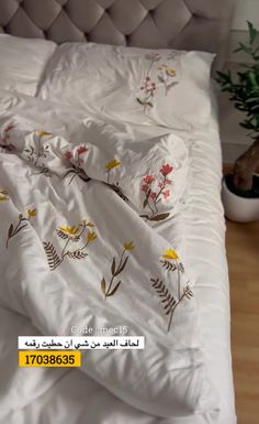 an unmade bed with white sheets and yellow flowers on it, next to a potted plant